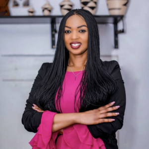 Delphine Uwamahoro profile pic, smiling at camera wearing black blazer over hot pink shirt with frilled sleeves, long hair in front of shoulders